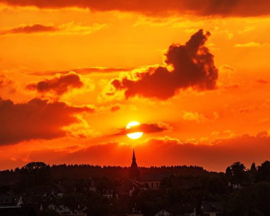 Diesen spektakulären Sonnenuntergang konnte man an Christi Himmelfahrt, 10. Mai 2018, in Drabenderhöhe beobachten. Um 20:46 Uhr stand die Sonne, von der Kronstädter Gasse aus gesehen, genau über der Kirchturmspitze. Foto: <a href="http://www.melzer.de">Günther Melzer</a>